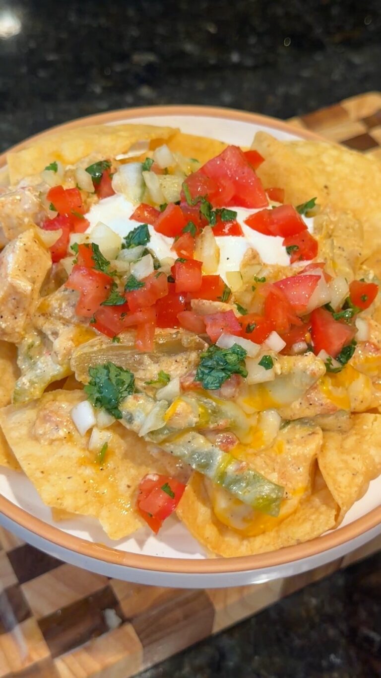 A plate of loaded nachos topped with melted cheese, chicken, sour cream, and fresh pico de gallo sits on a wooden board.