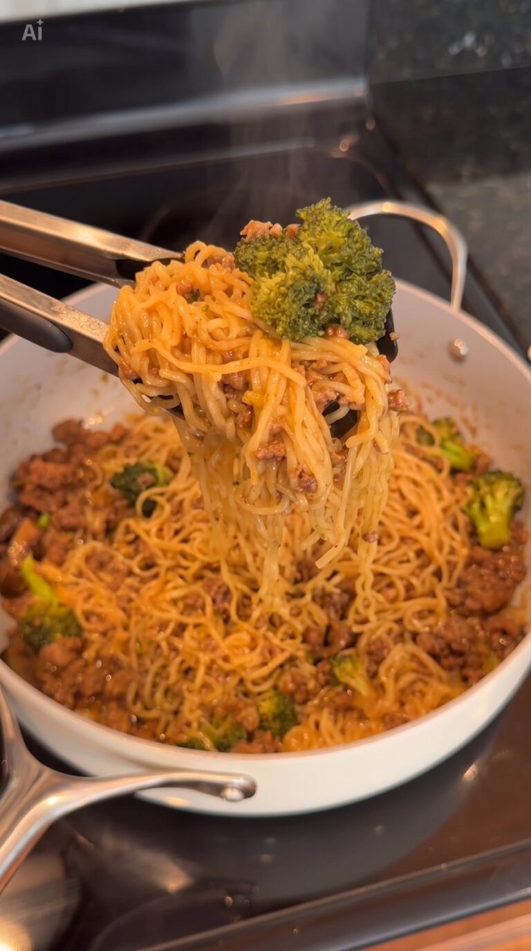 A pair of tongs lifts a serving of saucy spaghetti with ground meat and broccoli from a white skillet on a stove.