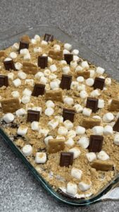 An overhead view of a baking dish filled with a s'mores dessert topped with marshmallows, graham crackers, and Hershey's chocolate bars.