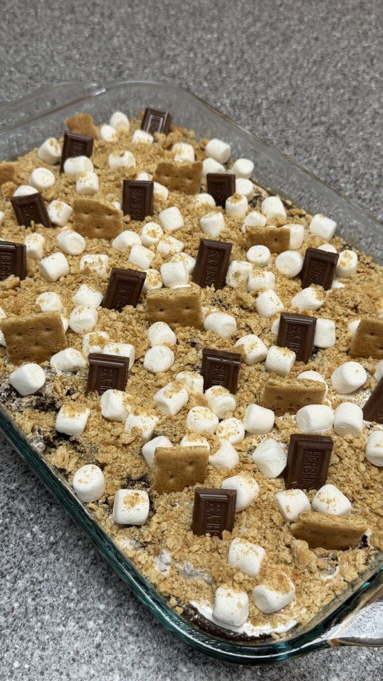 An overhead view of a baking dish filled with a s'mores dessert topped with marshmallows, graham crackers, and Hershey's chocolate bars.